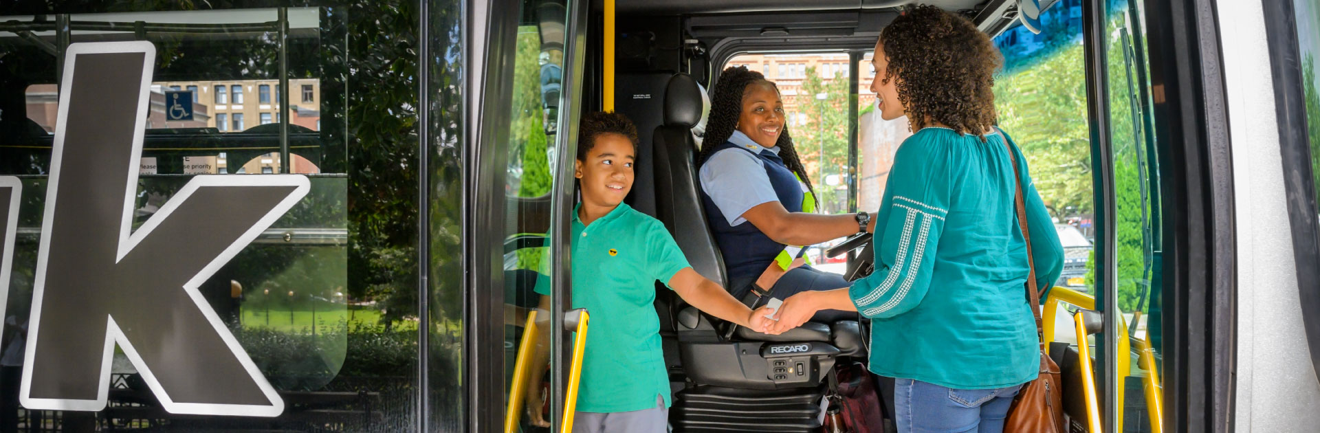 A woman and child board a bus. The bus driver is smiling at them.