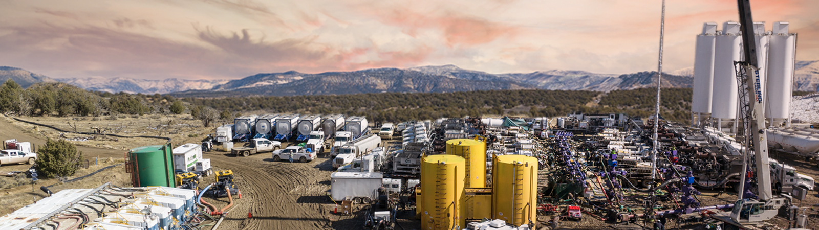 A hydraulic fracturing rig is shown in the foreground with mountains in the background.