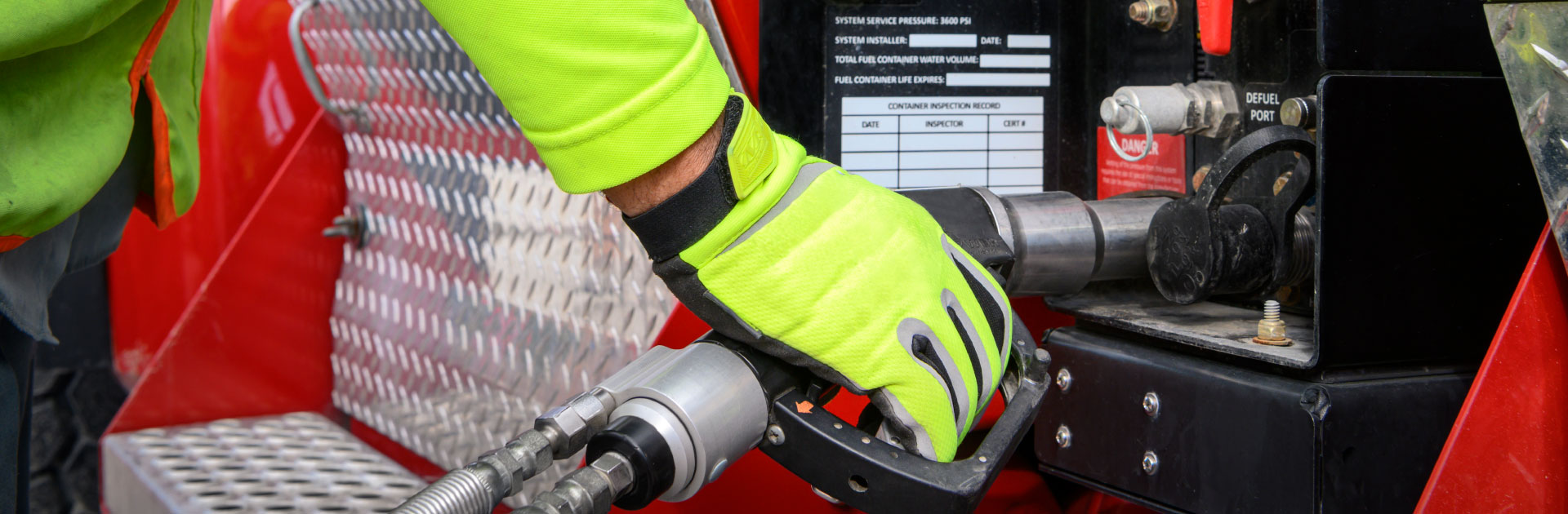 A yellow gloved hand holds a fuel hose up to a truck.