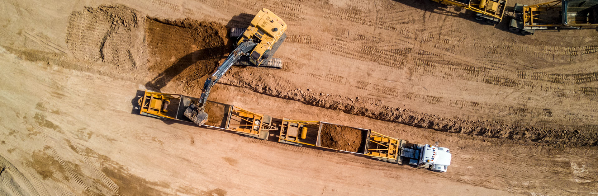 An aerial view of a bottom dump truck receiving a load of dirt from a backhoe.