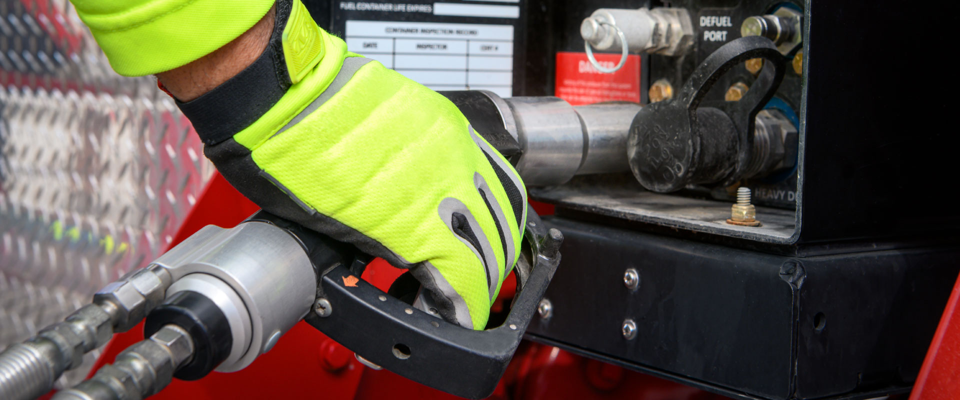A hand in a yellow glove grasps a fuel handle as it is placed into the fuel location in a vehicle.